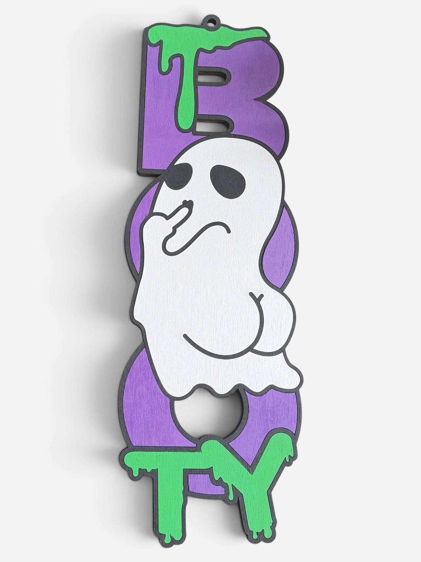 A Halloween-themed wooden ghost sign spelling 'BOO TY' in purple letters with green dripping paint accents and a cheeky ghost character in the center, shown against a plain light background.